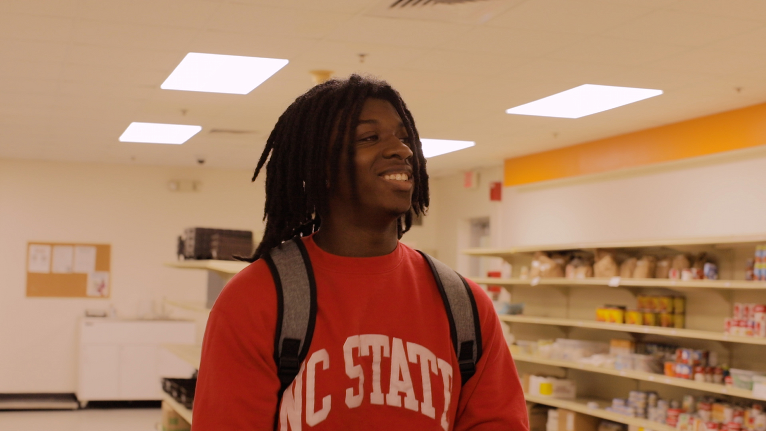 A smiling student walks the aisles of NC State's Feed the Pack food pantry.