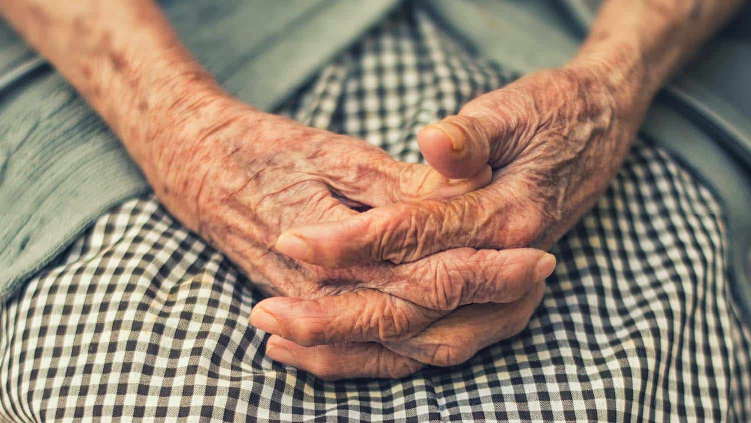 A person's aged hands are crossed and sit on their lap.